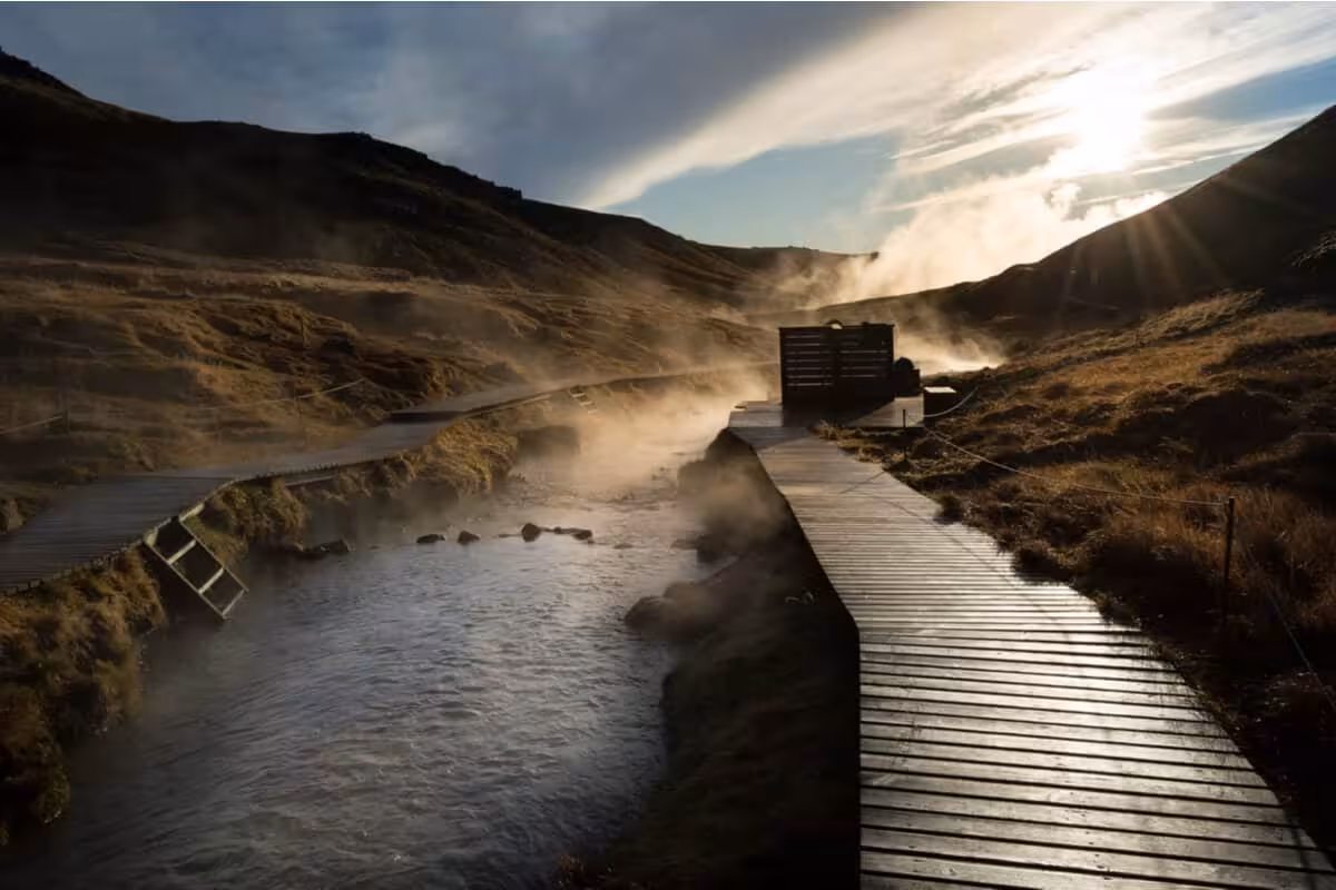 Steaming Reykjadalur hot river with wooden boardwalk path winding through Icelandic valley at sunset