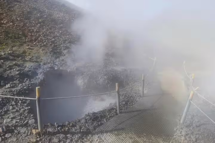 Steaming geothermal hot spring with rocky terrain and safety rope fence at Reykjadalur, Iceland