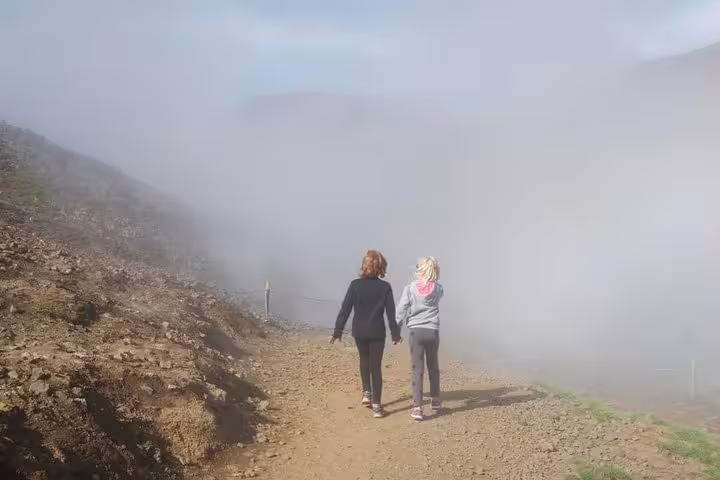 Two hikers walking hand in hand on a foggy mountain trail toward Reykjadalur hot spring river