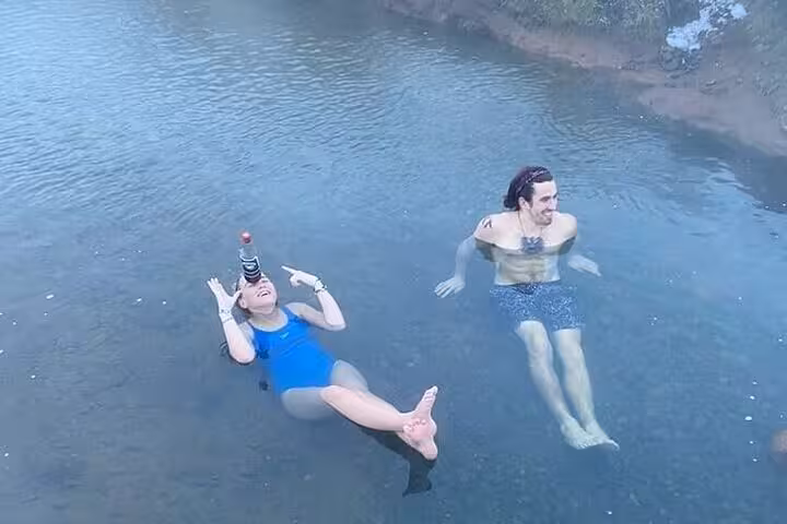 Two visitors floating and relaxing in the warm natural hot spring waters of Reykjadalur valley, Iceland