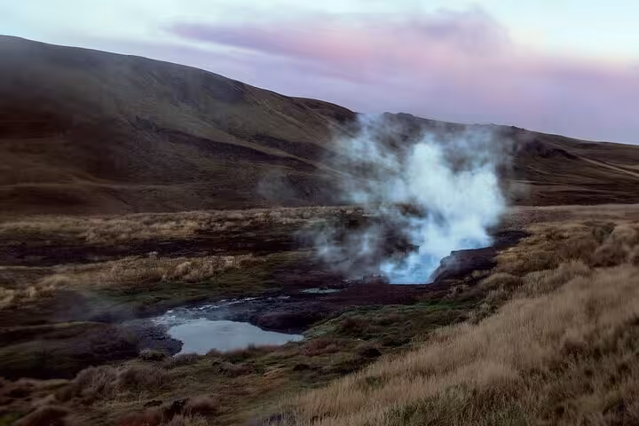 Steam rising from Reykjadalur hot springs geothermal area with golden grasslands and hills at dusk
