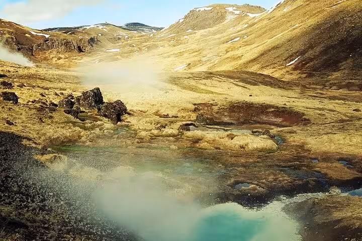 Steaming turquoise geothermal hot spring pool in Reykjadalur valley with misty volcanic landscape