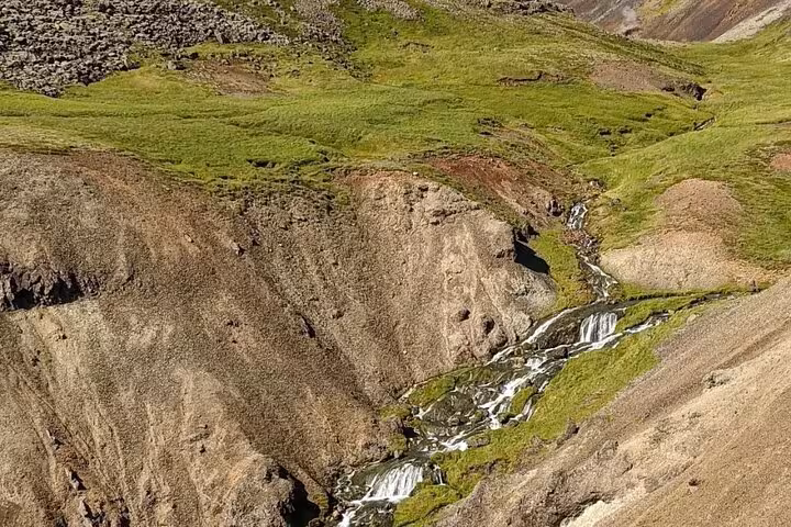 Cascading waterfall through green volcanic canyon at Reykjadalur hot springs hiking trail Iceland