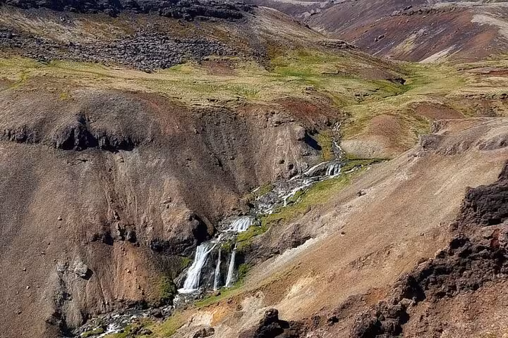 Cascading waterfalls flowing through a rugged volcanic canyon with green moss and reddish hills in Iceland