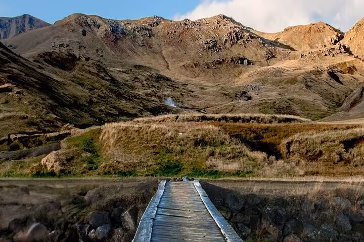 Wooden boardwalk leading to Reykjadalur hot springs valley with rugged Icelandic mountains backdrop