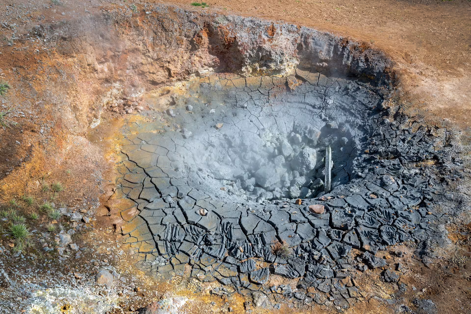 Steaming mud pot and cracked geothermal clay field on the private Reykjadalur hot river hike, Iceland
