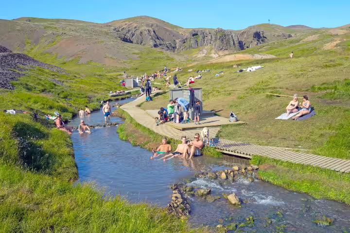 People enjoying a relaxing soak in the geothermal hot river amidst the scenic Reykjadalur Valley in Iceland.