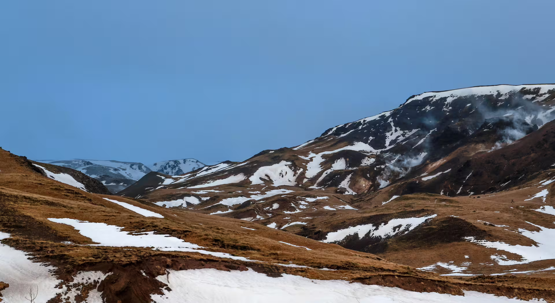Scenic view of Reykjadalur Valley with snowy peaks and geothermal steam, perfect for a hot river hiking adventure in Iceland.