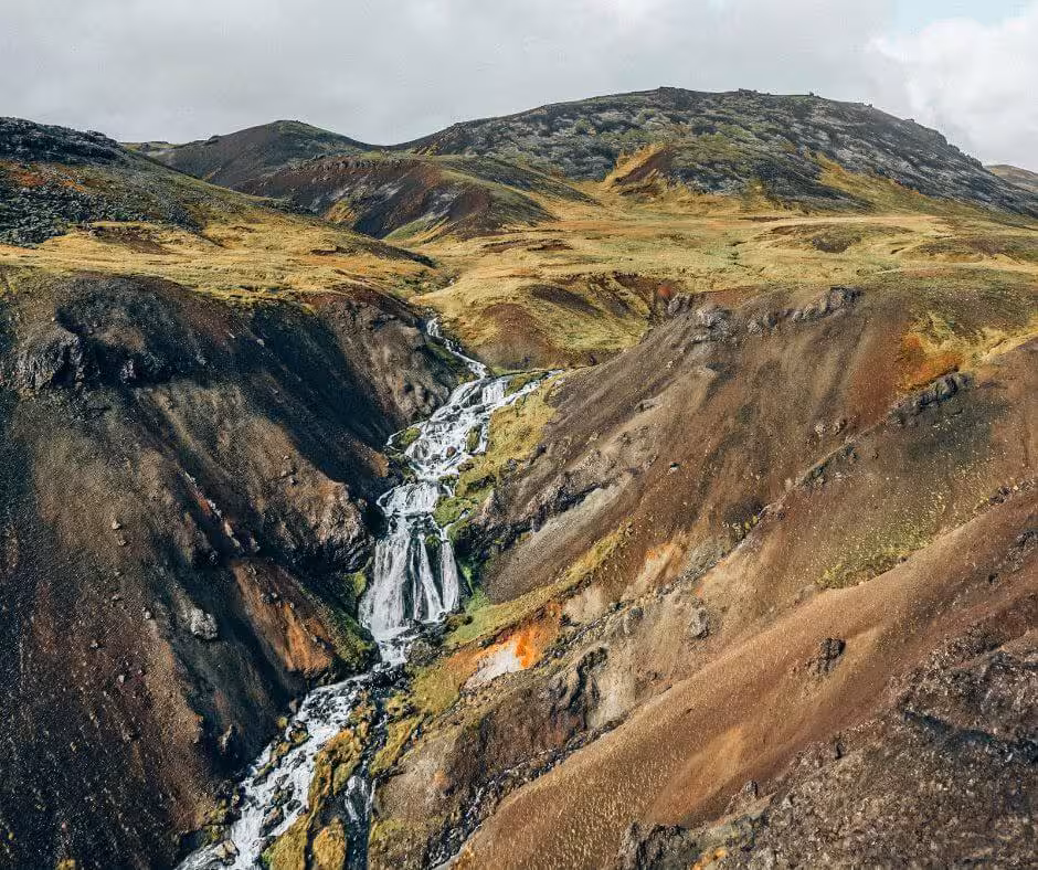 Cascading waterfall through colorful volcanic canyon at Reykjadalur valley in Iceland