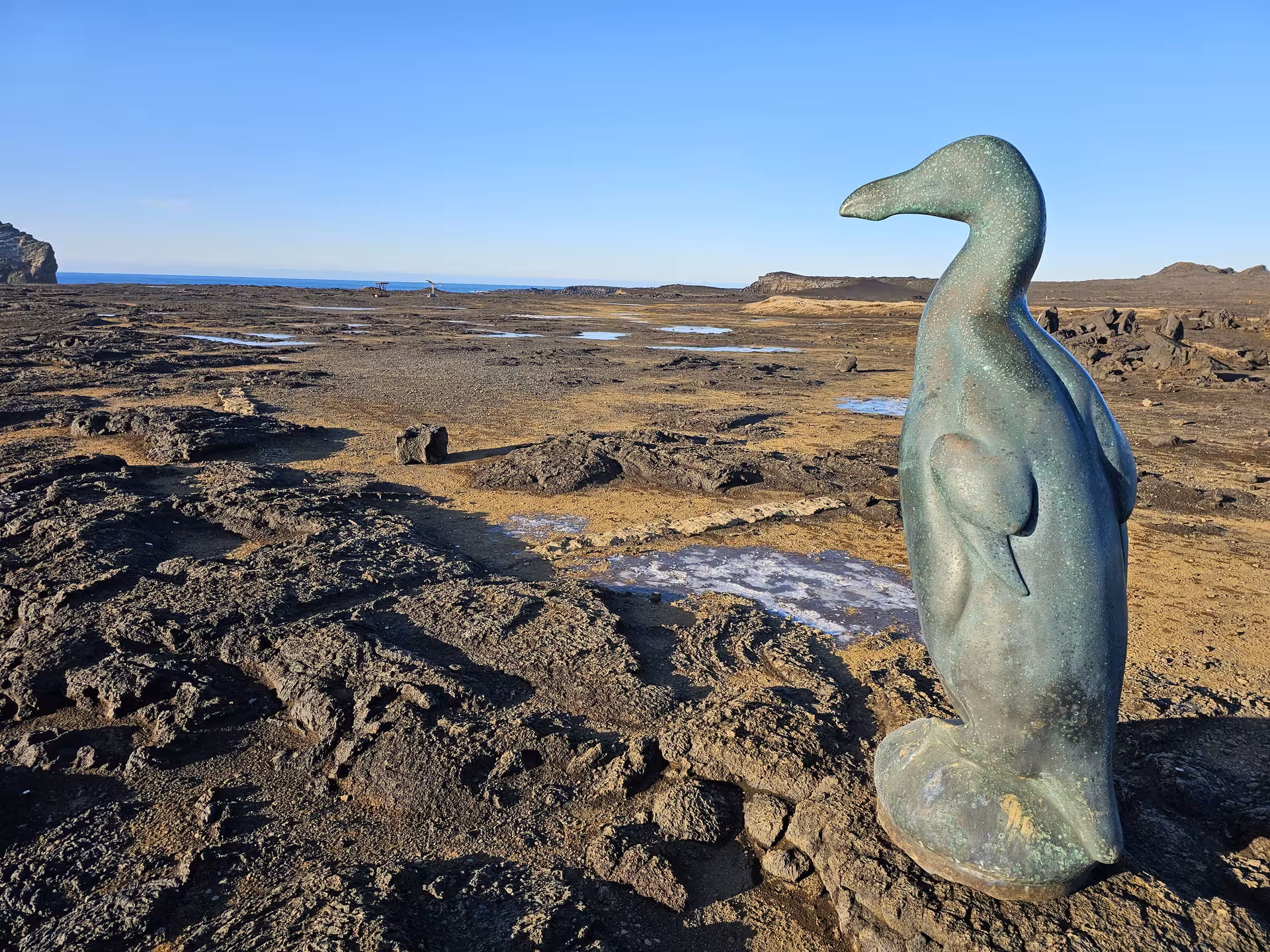Bronze penguin statue on volcanic lava rock coastline at Reykjanes Geopark, Iceland