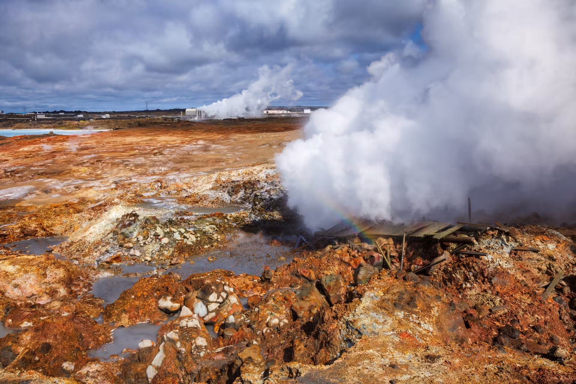 Steaming geothermal vents with colorful mineral-stained rocks and geothermal plant in Reykjanes Geopark, Iceland