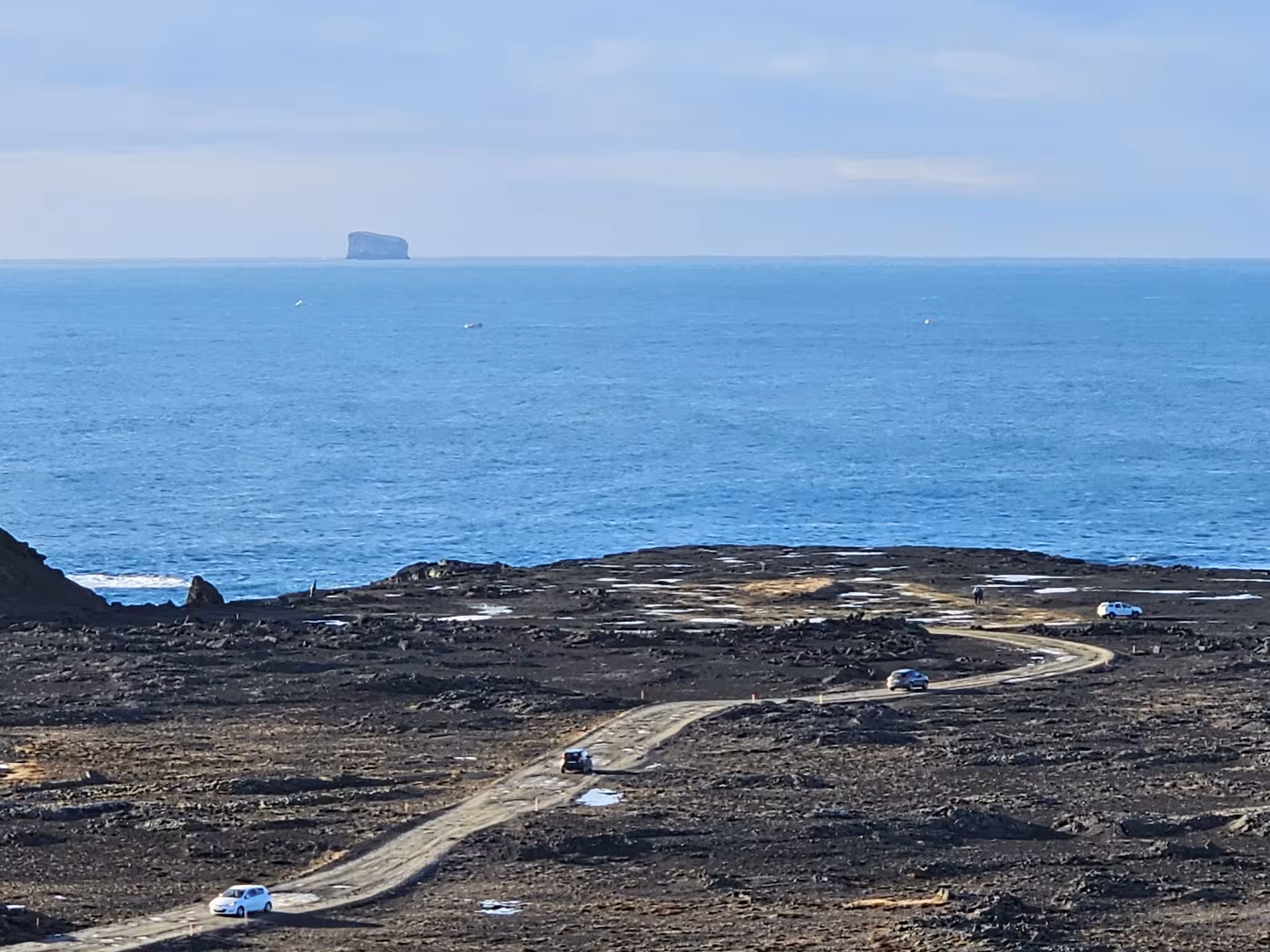 Winding gravel road through Reykjanes lava fields with ocean and distant rock island in background