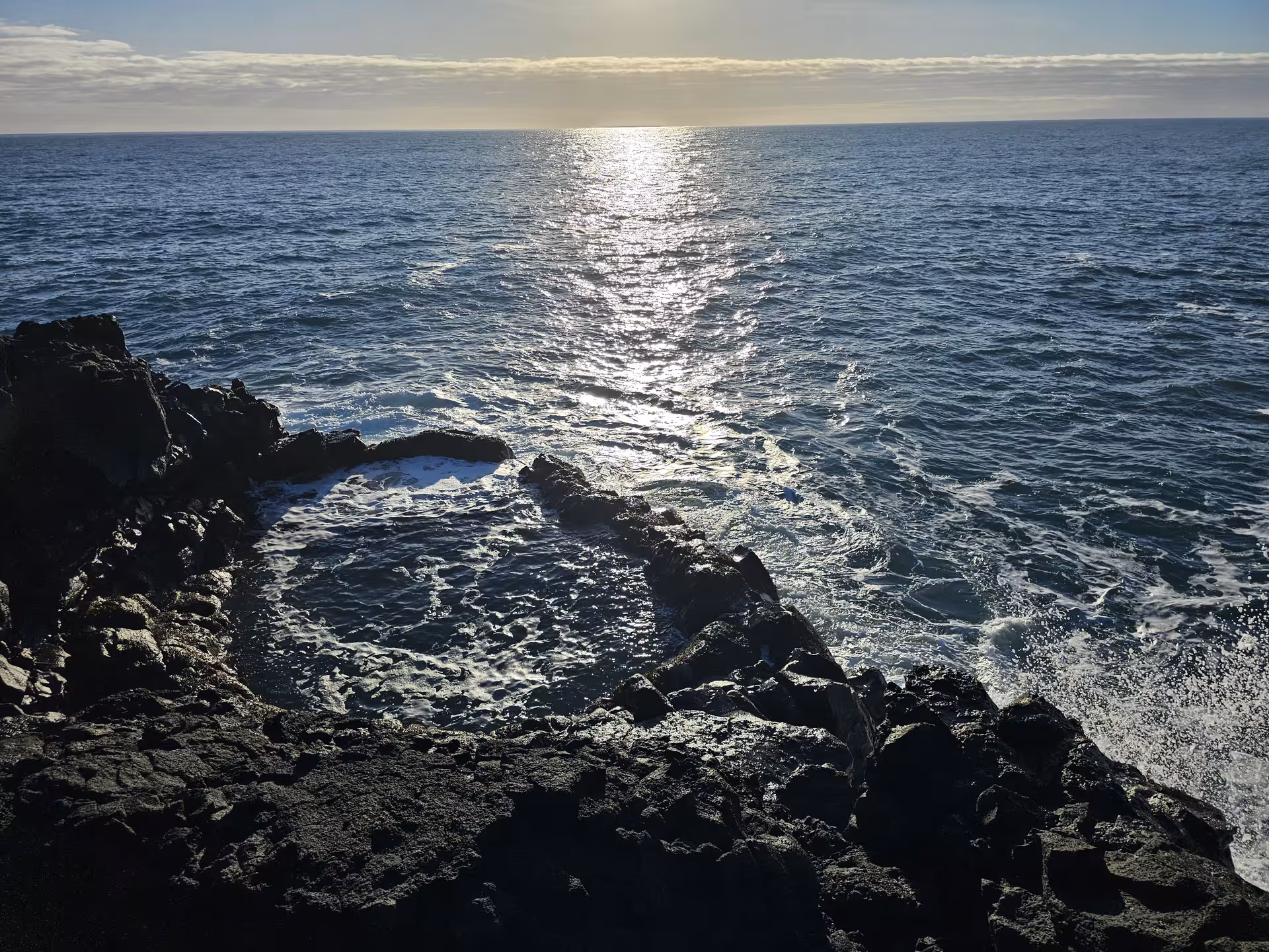 Rocky lava coastline with sunlight reflecting on the ocean at Reykjanes Geopark, Iceland