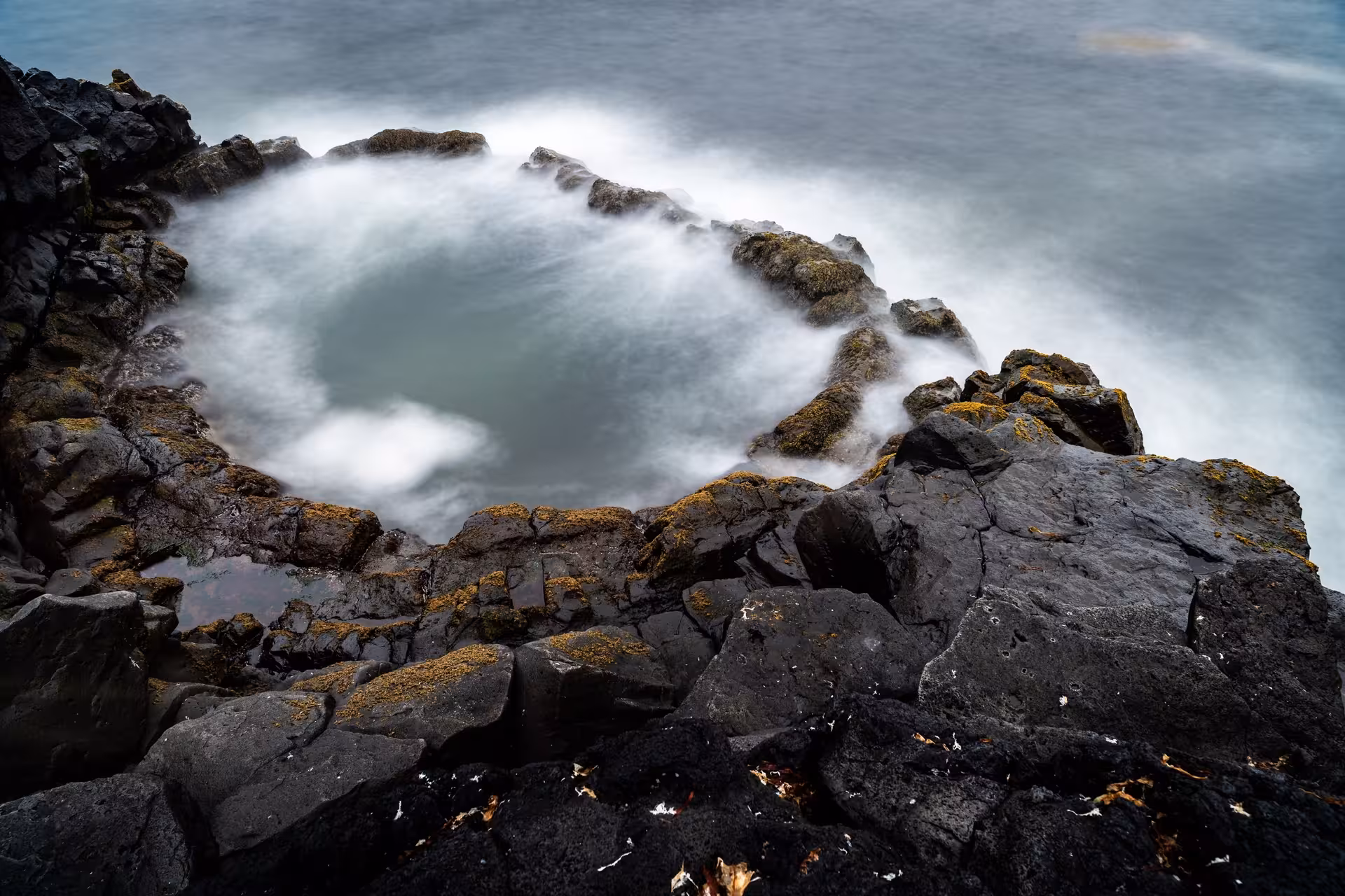 Circular lava rock tidal pool with silky white waves at Reykjanes Geopark Iceland coastline