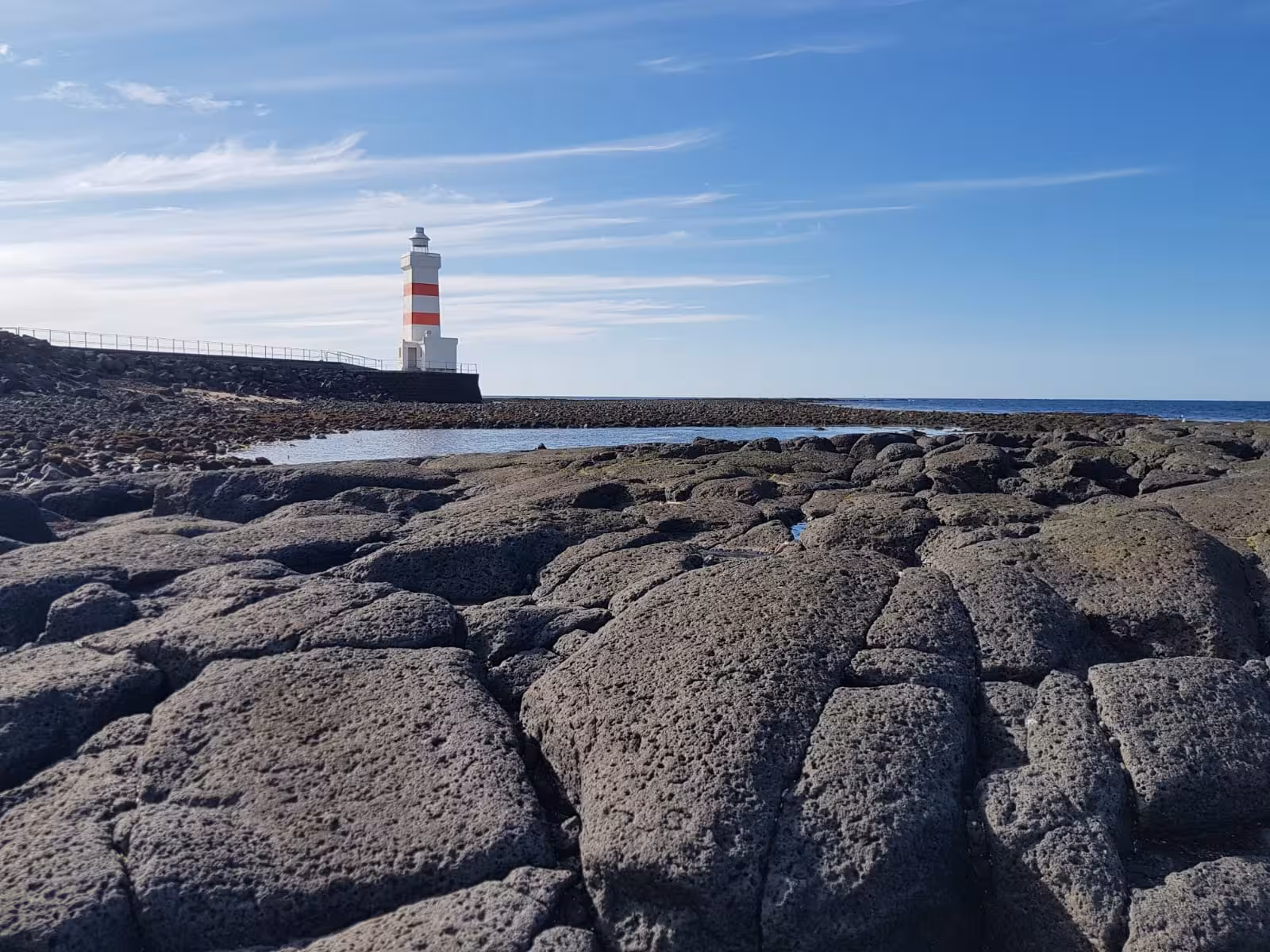 Red and white striped lighthouse on volcanic lava rock coastline at Reykjanes Geopark, Iceland