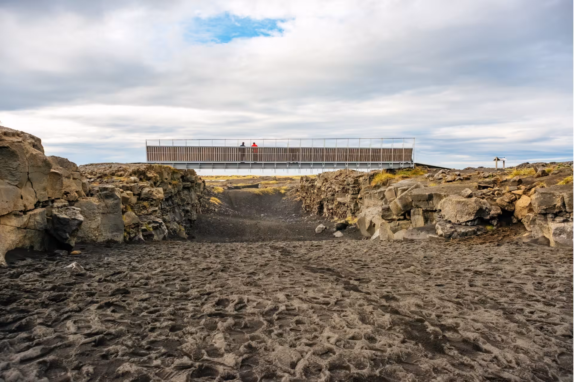 Bridge spanning tectonic plate rift at Reykjanes Geopark with visitors overlooking volcanic landscape