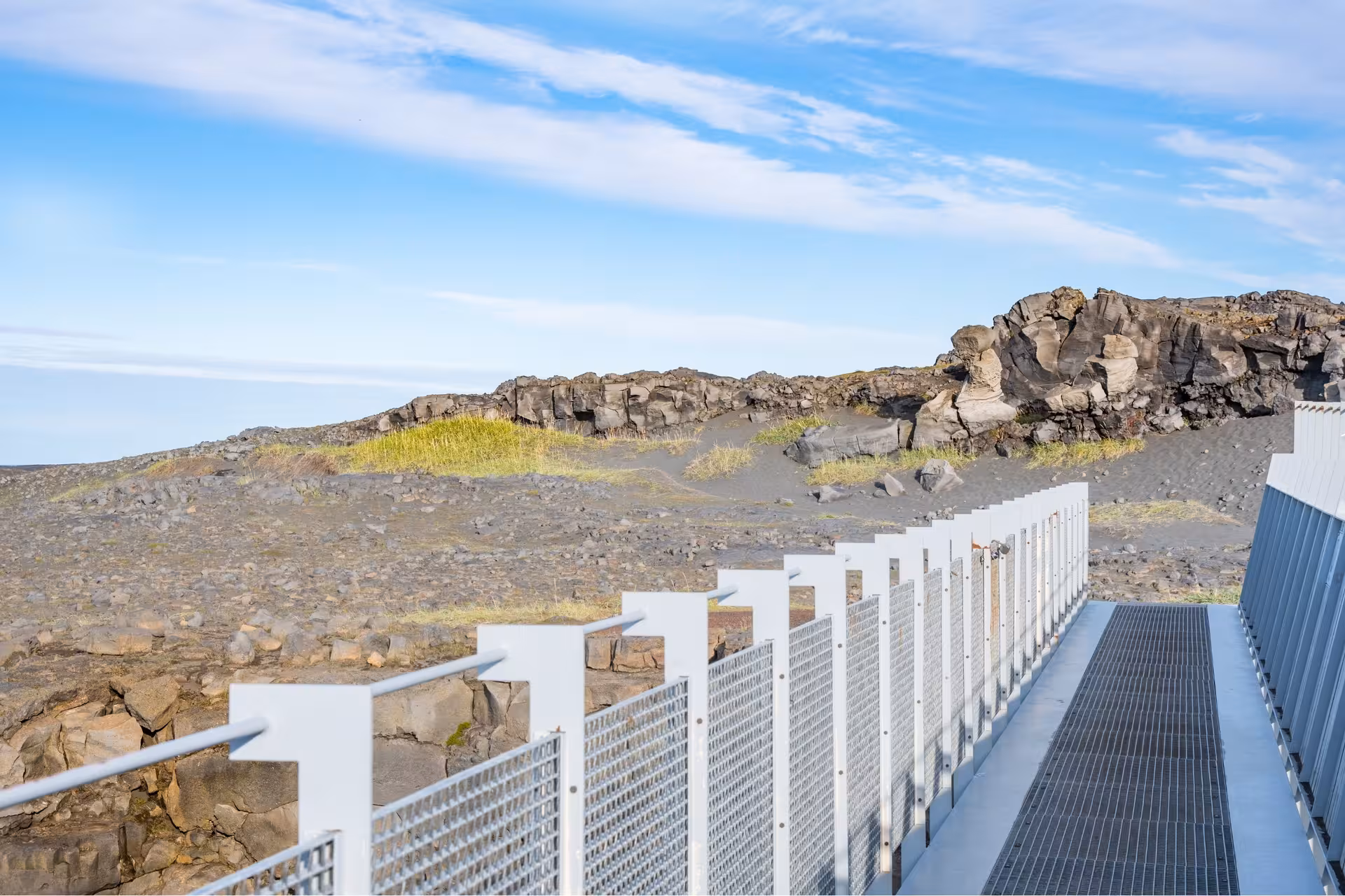 Metal walkway overlooking black volcanic lava fields and rocky formations at Reykjanes Geopark, Iceland