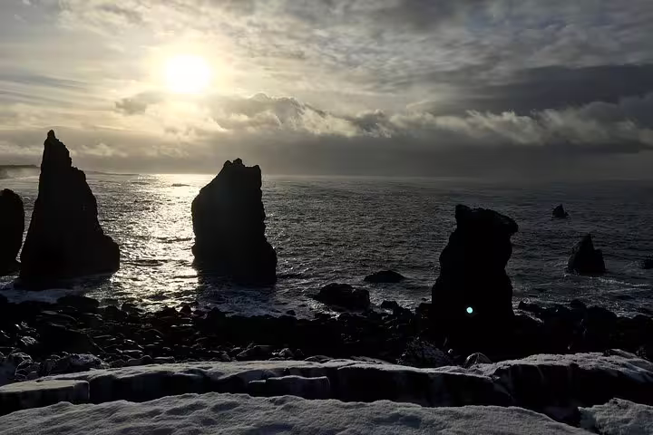 Dramatic volcanic sea stacks silhouetted against a glowing sunset over the icy Atlantic Ocean in Reykjanes, Iceland
