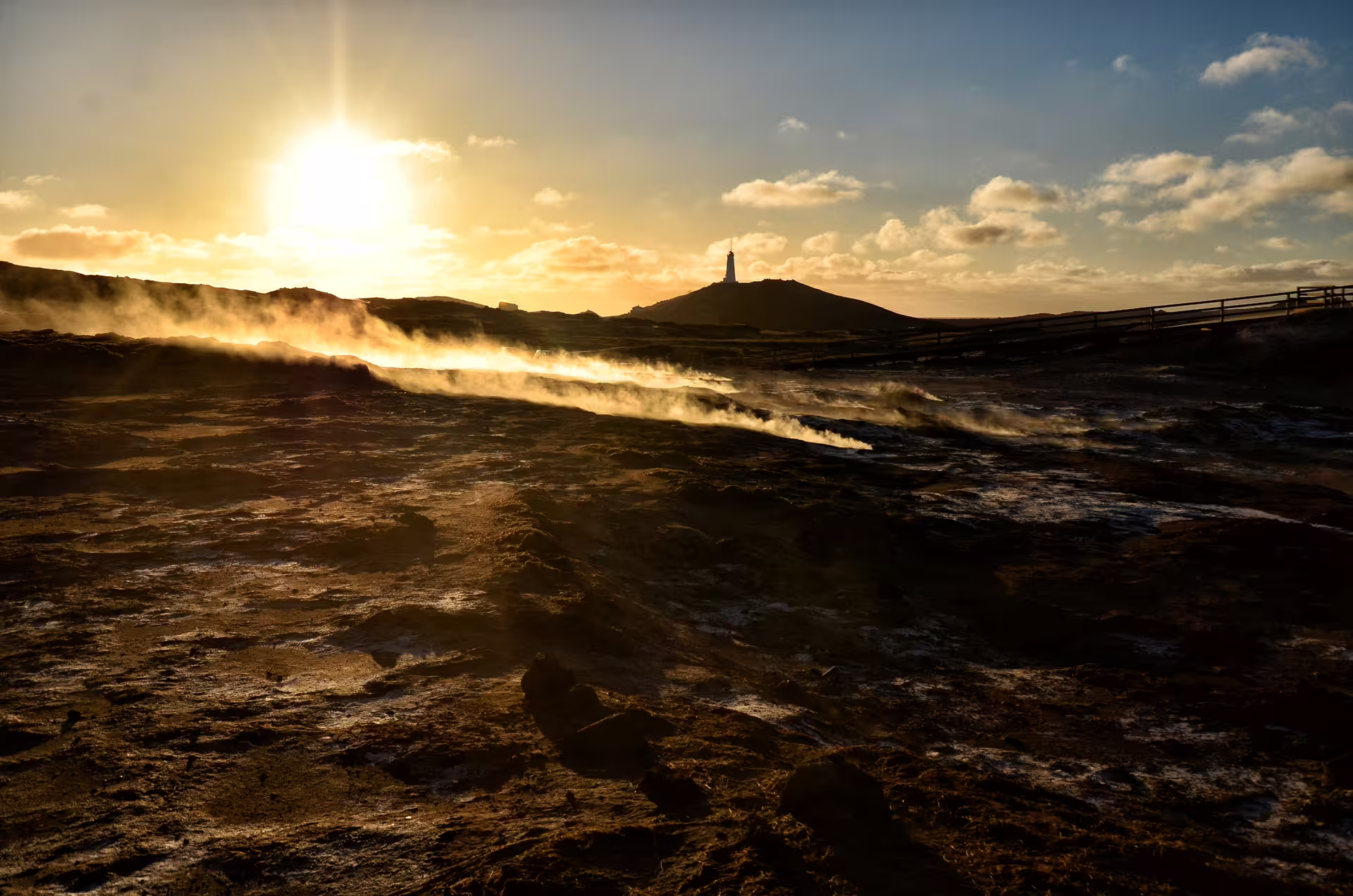 Geothermal steam rising over lava fields at golden sunset near Reykjanes lighthouse, Iceland