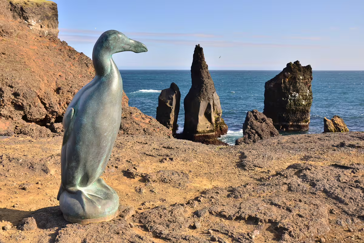 Bronze great auk statue on volcanic rocky cliffs with dramatic sea stacks and ocean at Reykjanes Peninsula