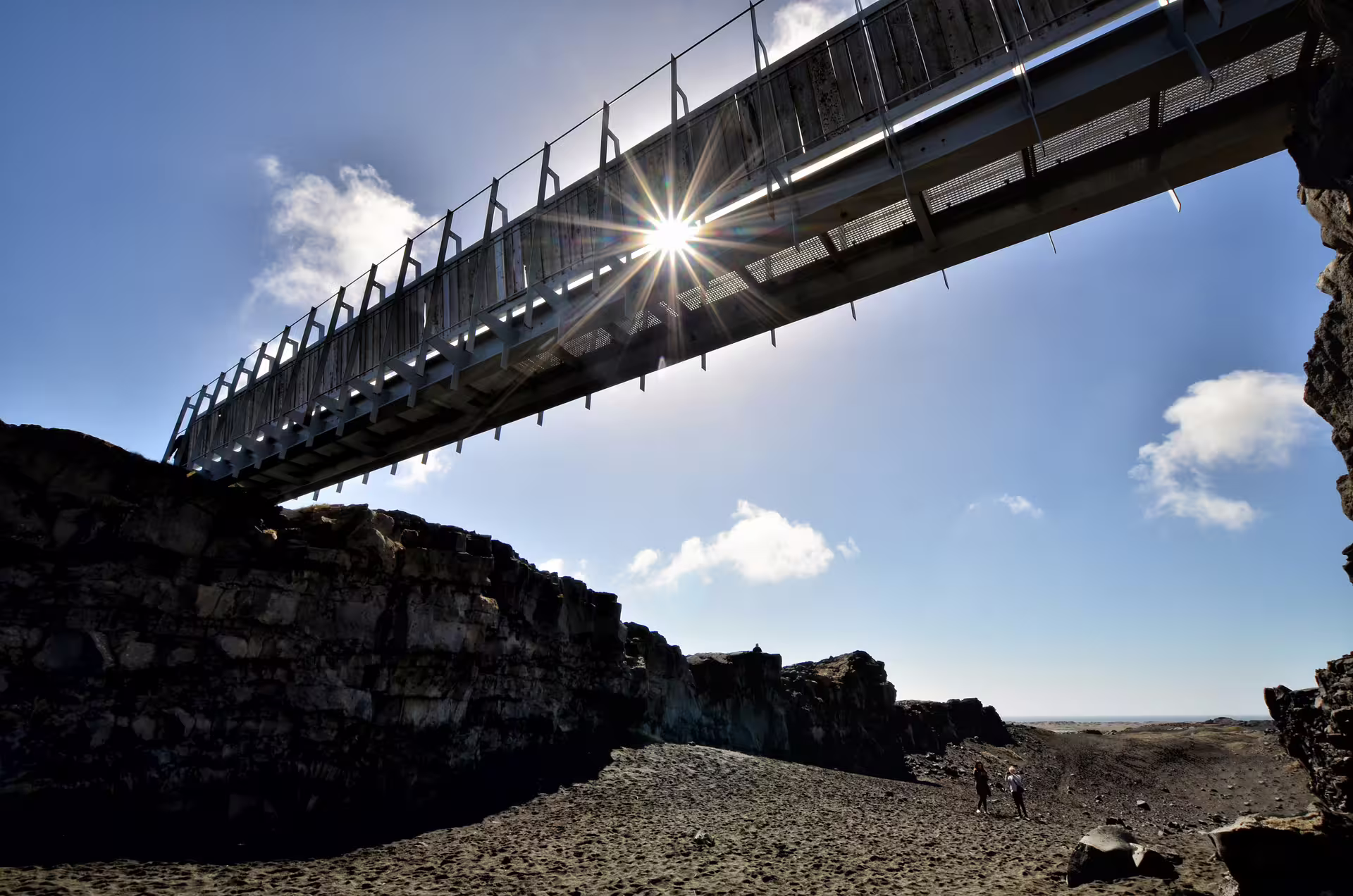 Metal footbridge over volcanic lava field canyon in Reykjanes Peninsula, Iceland, with sun flare