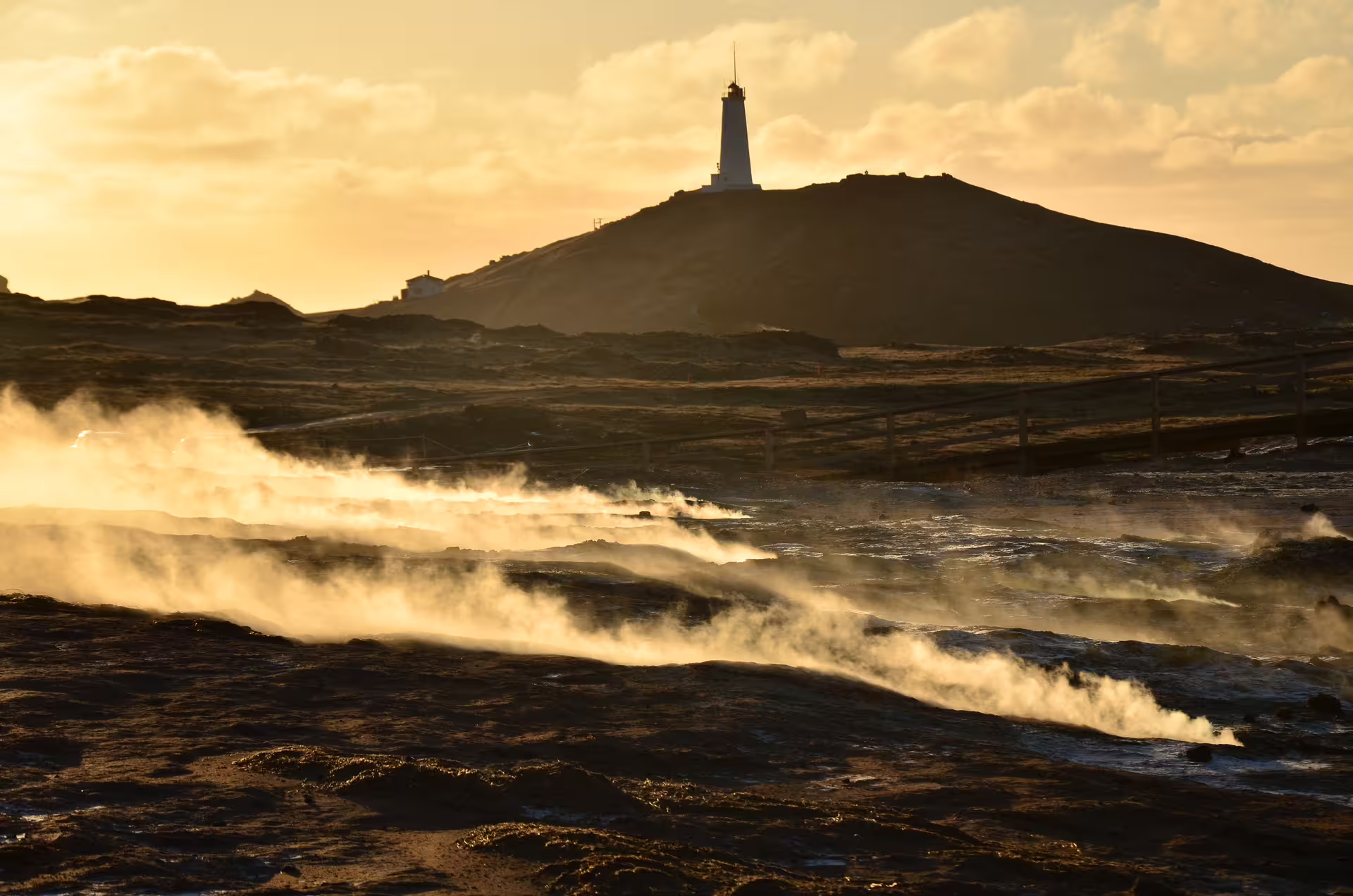 Geothermal steam rising over lava fields at golden sunset with lighthouse on Reykjanes Peninsula, Iceland