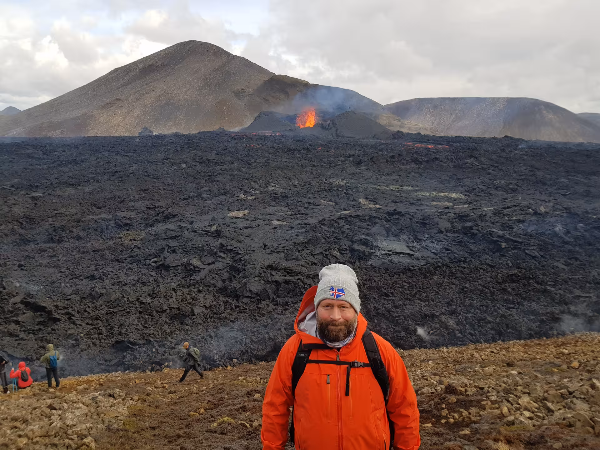 Tourist in orange jacket posing in front of active volcanic eruption on Reykjanes Peninsula, Iceland