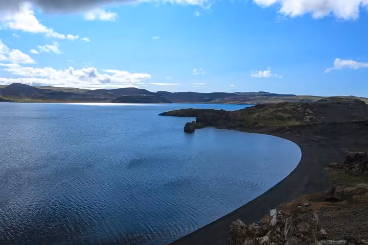 Black sand beach along a calm blue lake surrounded by volcanic hills on the Reykjanes Peninsula, Iceland