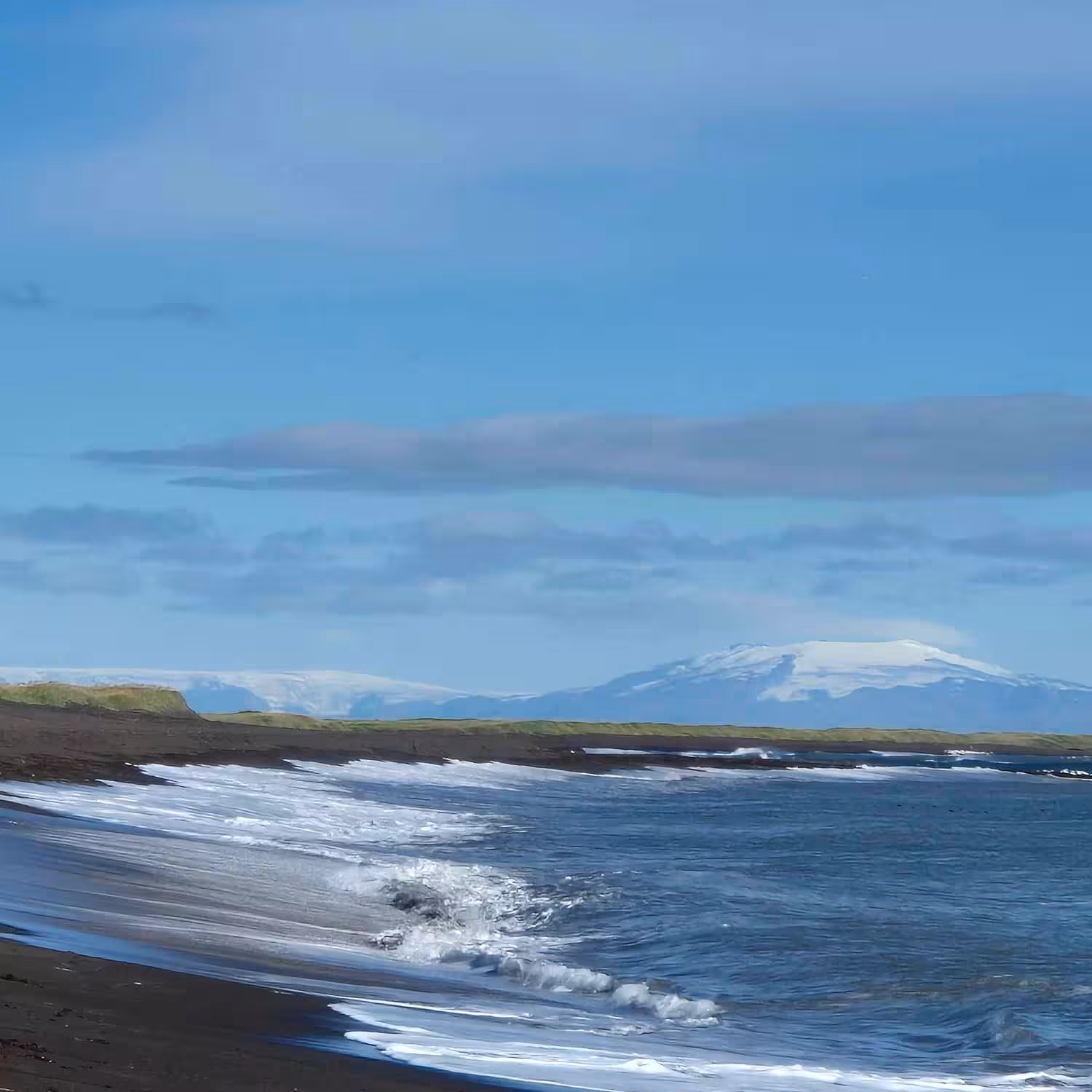 Black sand beach with waves and snow-capped volcano on Reykjanes Peninsula, Iceland