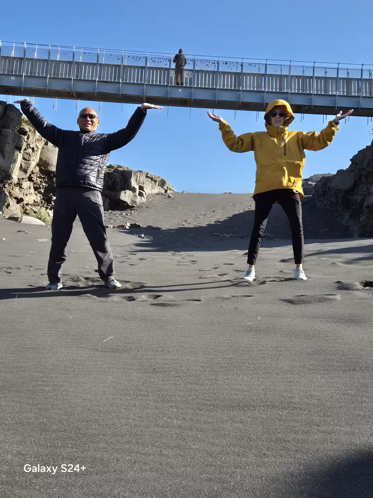 Two tourists posing playfully on black sand beach under bridge on Reykjanes Peninsula Iceland