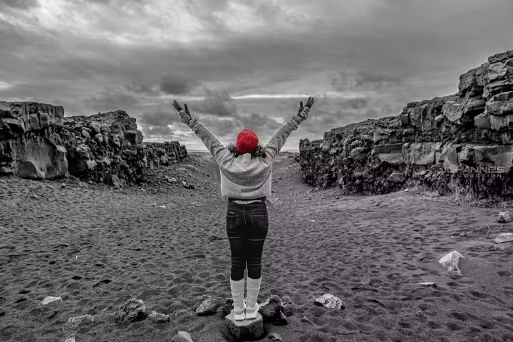 Traveler with arms raised on black sand beach, Reykjanes Peninsula, Iceland