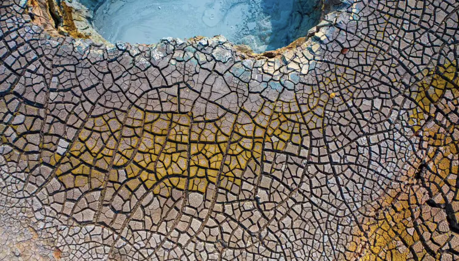 Aerial view of cracked dry earth surrounding a blue geothermal pool on the Reykjanes Peninsula, Iceland