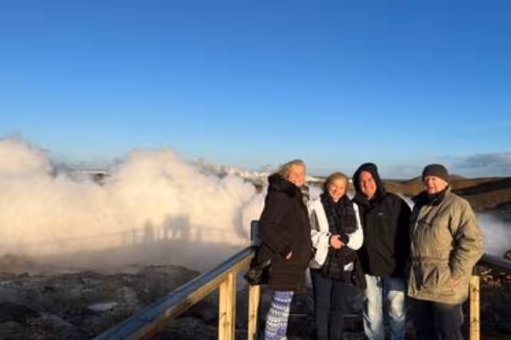Four tourists posing on wooden viewing platform with geothermal steam vents on Reykjanes Peninsula