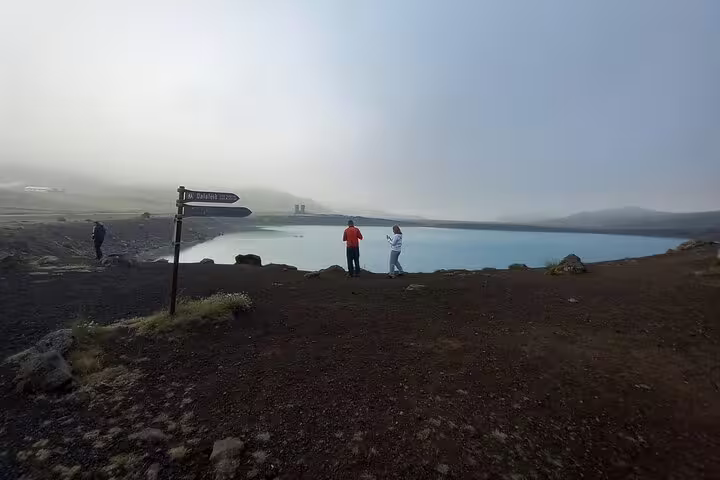 Tourists standing beside a vivid blue geothermal lake on the misty Reykjanes Peninsula lava fields