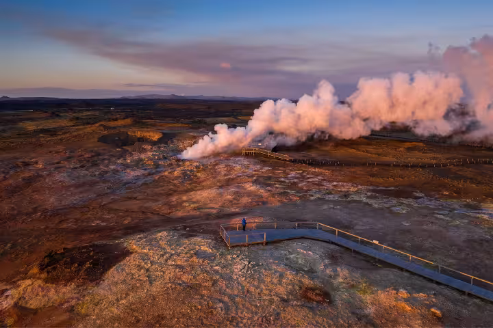 Aerial view of geothermal steam vents on Reykjanes Peninsula at sunset with lone visitor on boardwalk