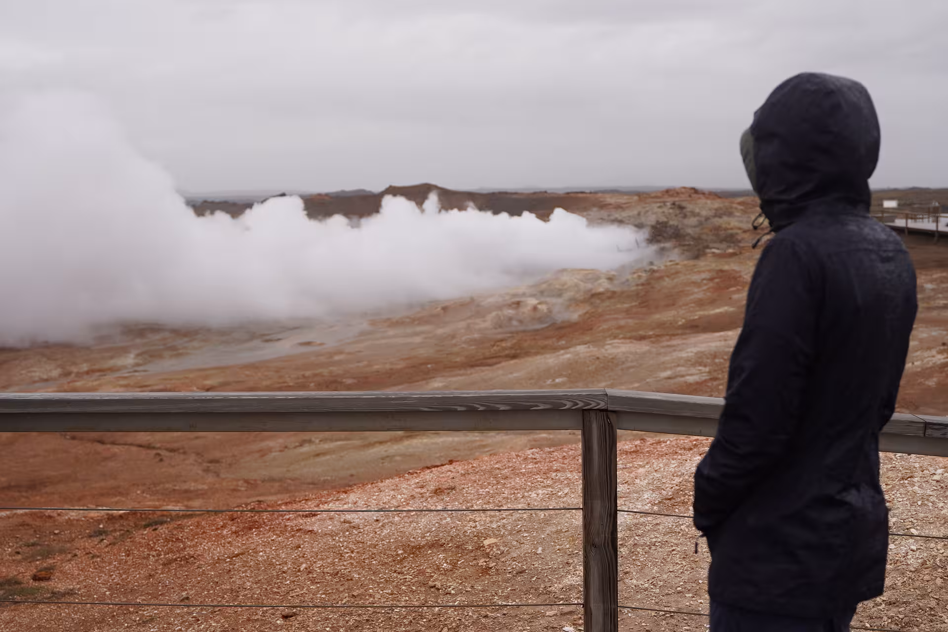 Hooded traveler overlooking steaming geothermal vents on Reykjanes Peninsula, Iceland