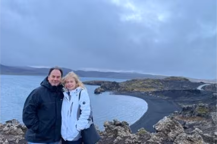 Couple posing at black sand beach on Reykjanes Peninsula with dramatic volcanic coastline and overcast sky