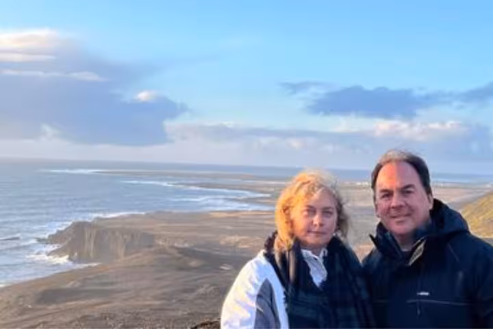 Couple posing on Reykjanes Peninsula cliffs with black sand beach and ocean views behind them