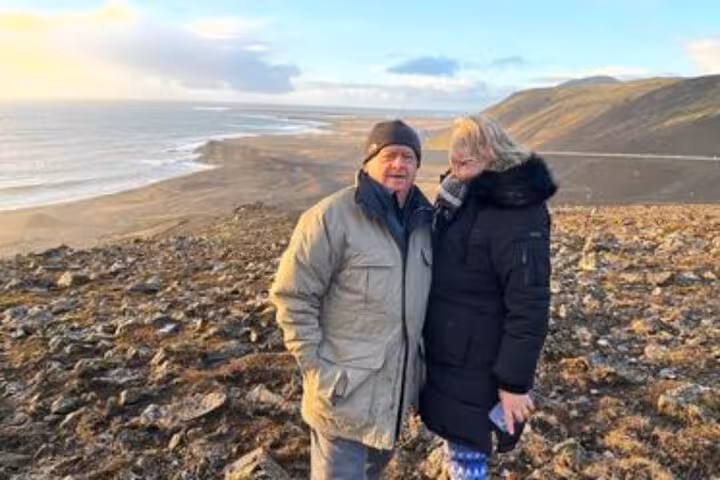 Couple in winter jackets standing on rocky Reykjanes Peninsula hillside overlooking Icelandic coastline