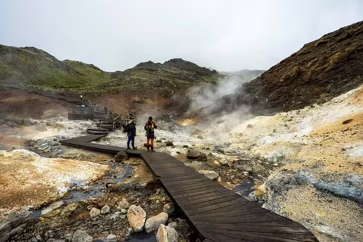 Two hikers on wooden boardwalk amid steaming geothermal hot springs on Reykjanes Peninsula, Iceland
