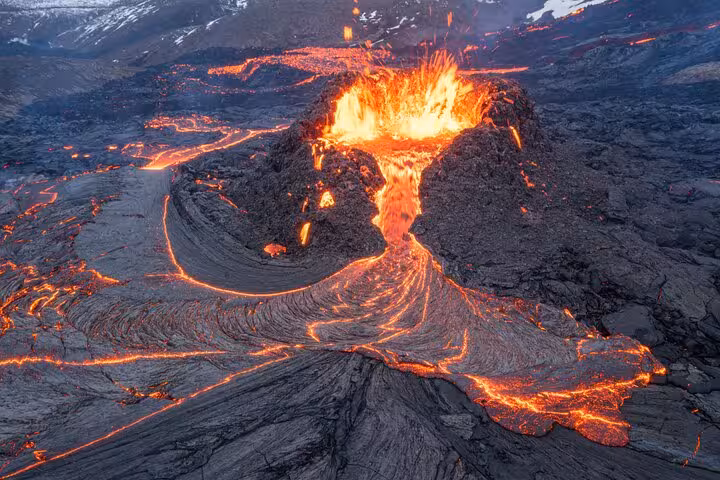 Active volcano erupting with glowing lava flows across dark rocky terrain in Reykjanes Peninsula, Iceland