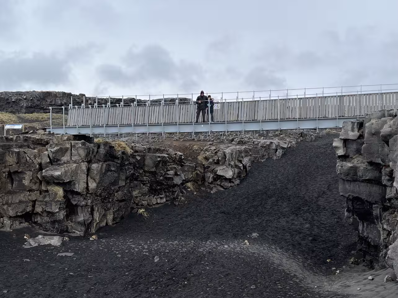 Tourists on bridge over black lava rock fissure on Reykjanes Peninsula, Iceland