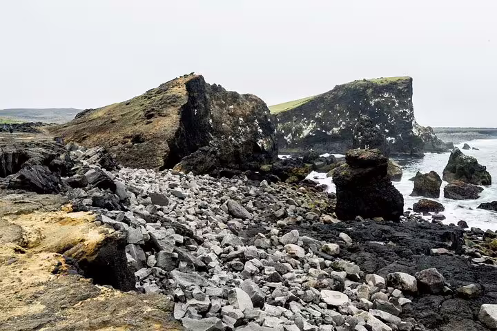 Rocky lava coastline with black volcanic rocks and green-capped sea cliffs on Reykjanes Peninsula, Iceland