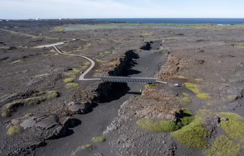 Aerial view of Reykjanes Peninsula lava fields with a bridge crossing a volcanic fissure near the ocean