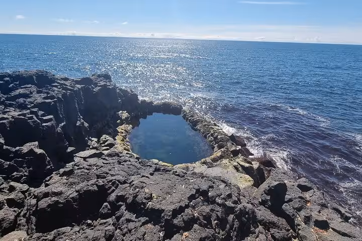 Natural lava rock tidal pool on Reykjanes Peninsula coastline with Atlantic Ocean in background