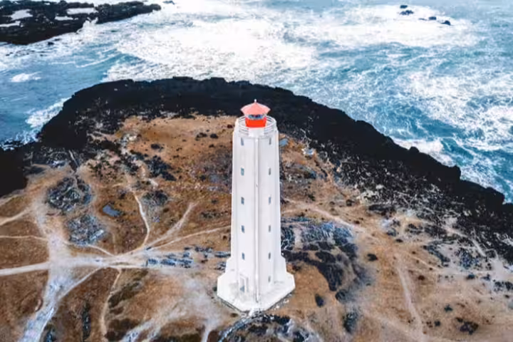 Aerial view of white lighthouse with red top on rocky Reykjanes Peninsula coastline, Iceland