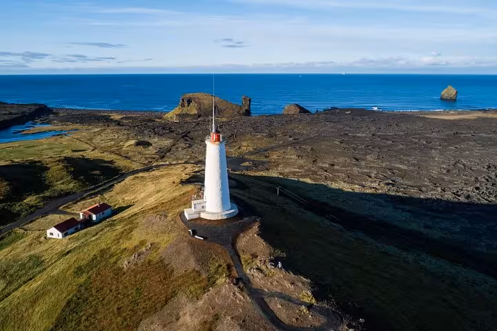 Aerial view of a white lighthouse on Reykjanes Peninsula coastline with rocky lava fields and blue ocean