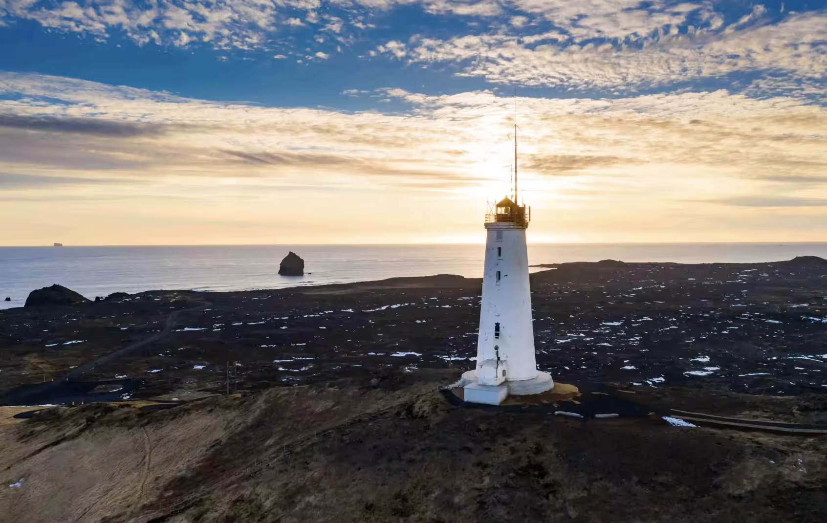 White lighthouse on Reykjanes Peninsula coastal lava field at golden sunset with ocean views