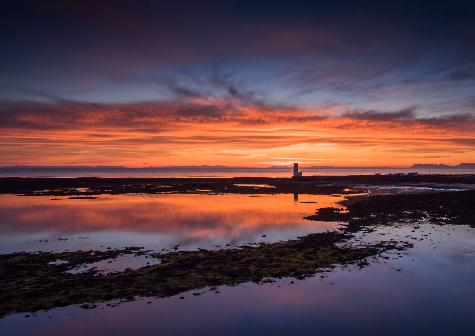 Dramatic red and orange sunset reflecting on tidal pools near a lighthouse on Reykjanes Peninsula, Iceland
