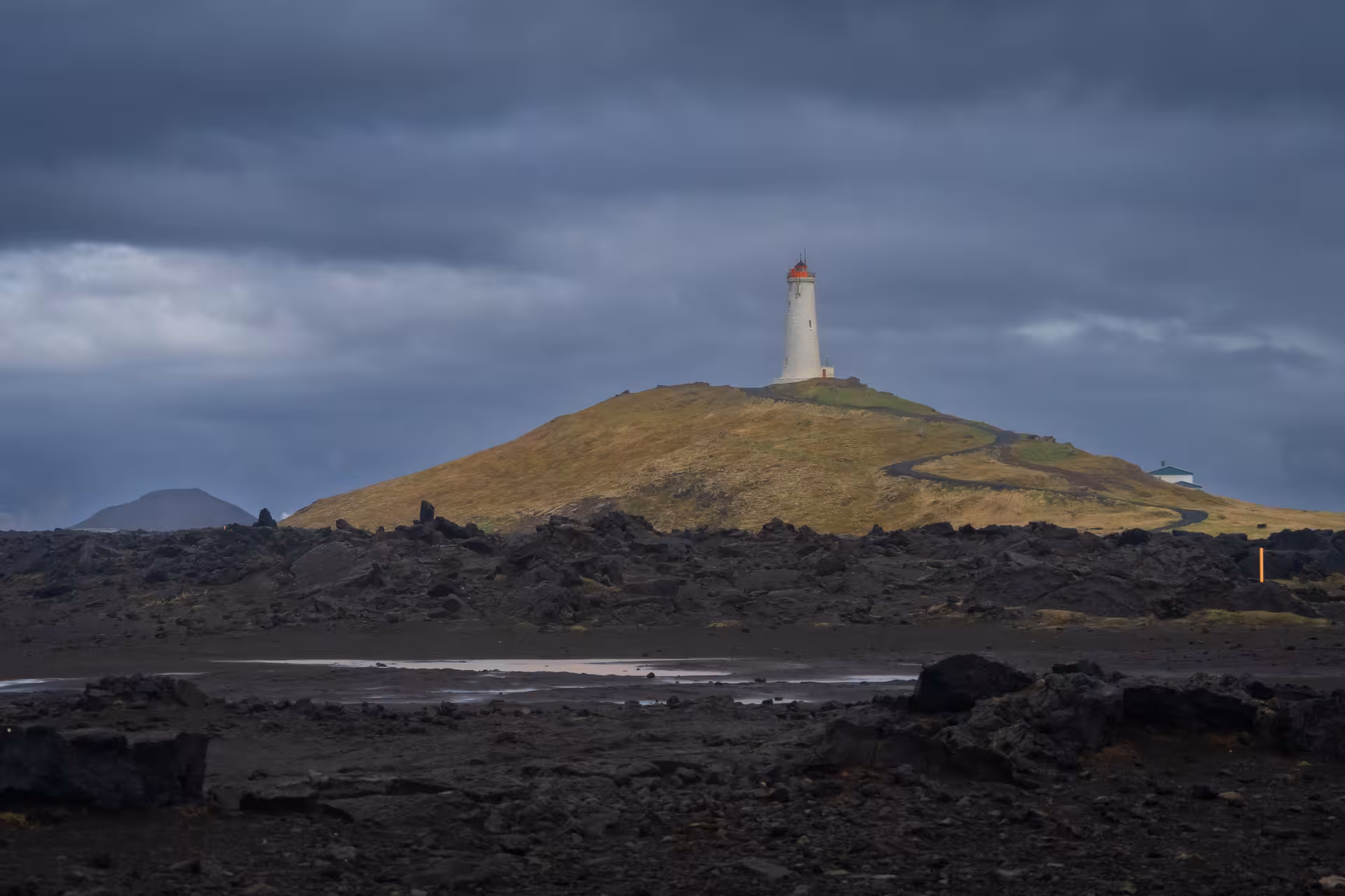 White lighthouse with red top on volcanic hill, Reykjanes Peninsula Iceland under dramatic stormy sky
